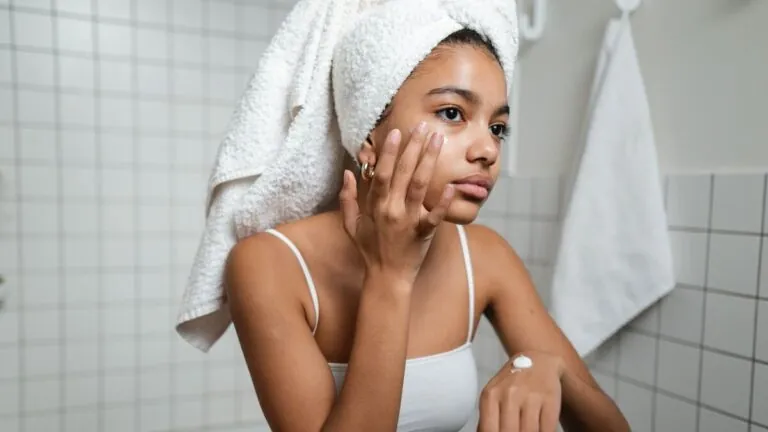 Woman with hair towel gently applying moisturiser to her face
