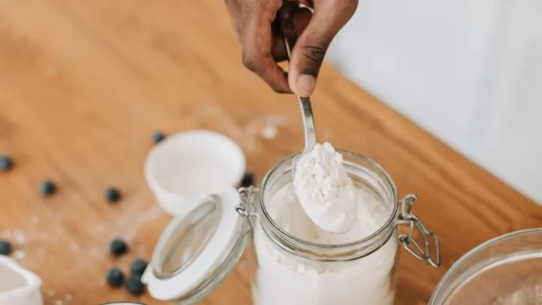 Spoon scooping white protein powder from a glass jar
