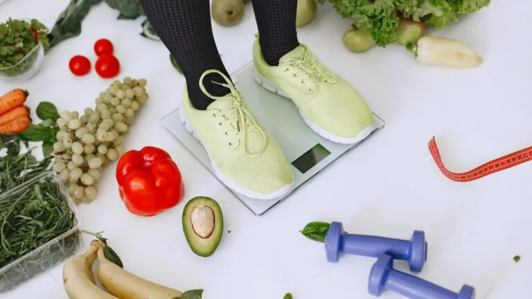 Person on a bathroom scale surrounded by vegetables and dumbbells