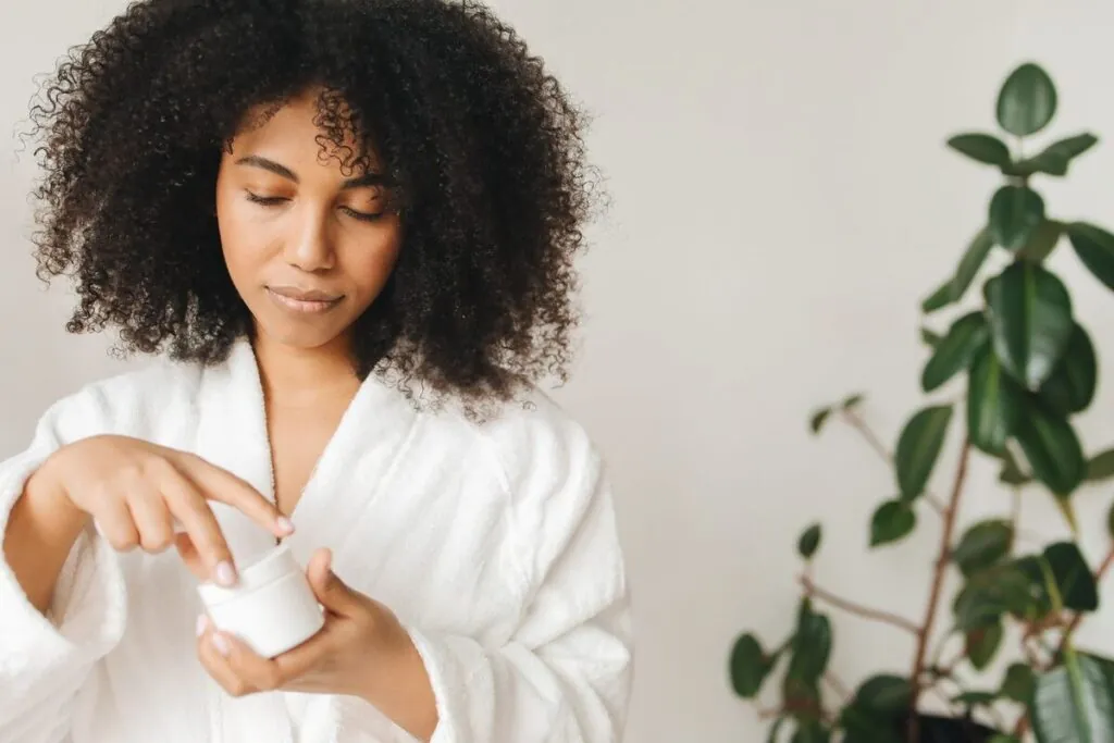 Woman with coily hair scooping curl cream from a jar