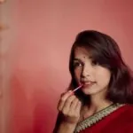Indian woman in a red saree applying lipstick