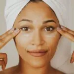 Woman in a towel wrap tapping under eye cream along her under-eye area