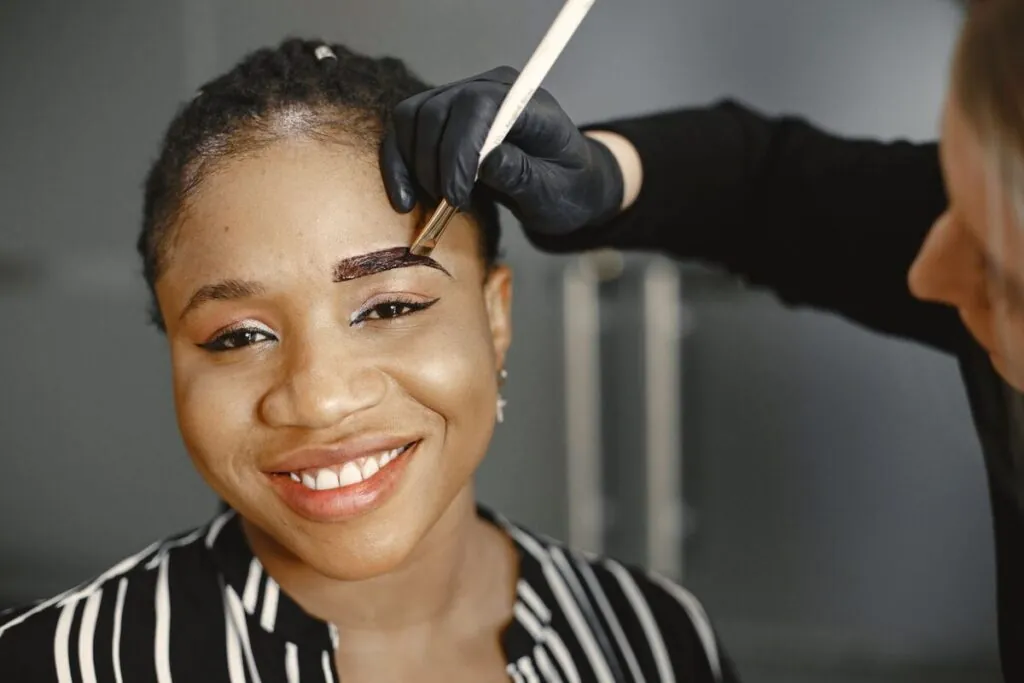 Makeup artist shaping a smiling woman's eyebrows with a brush