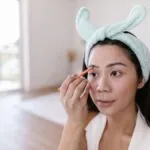 Woman with a headband filling in her eyebrows with a pencil