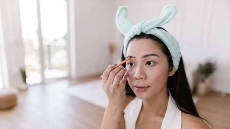 Woman with a headband filling in her eyebrows with a pencil