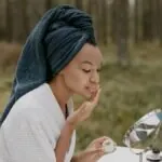 Woman in a robe applying cream to her face outdoors