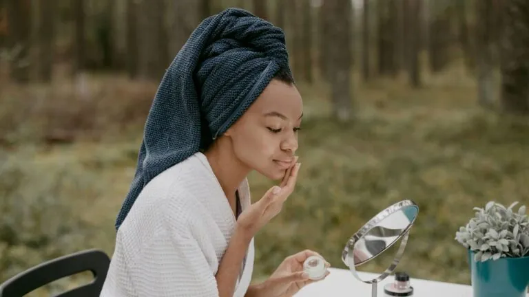 Woman in a robe applying cream to her face outdoors