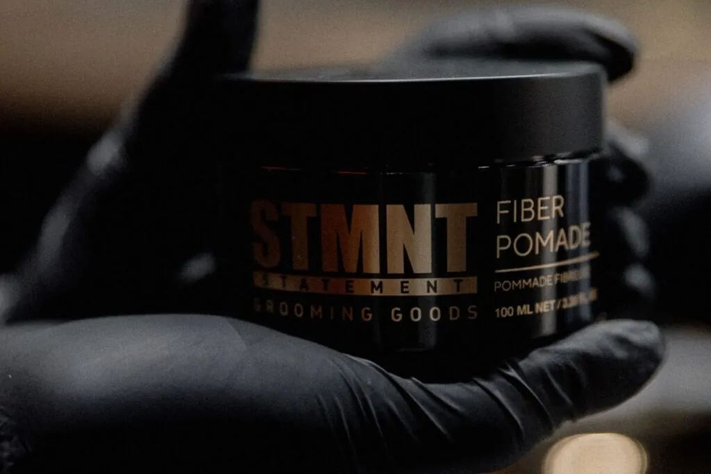Gloved hand holding a tub of men's fibre pomade