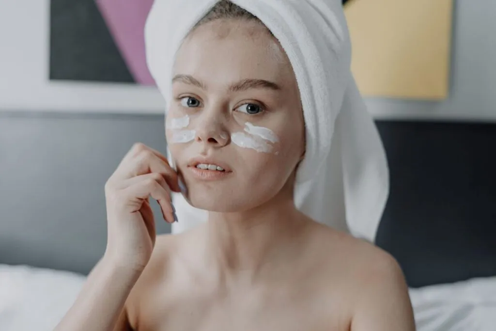 Woman applying moisturiser to her face with a towel on her head