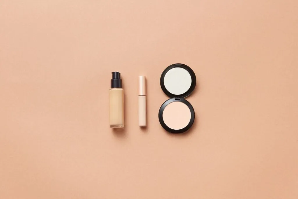 Foundation, concealer and compact powder on a peach background
