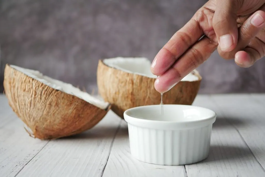 Coconut oil dropped into a small bowl beside coconut halves