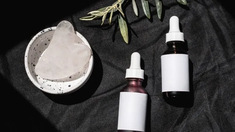 Skincare serum dropper bottles and a gua sha on a dark cloth