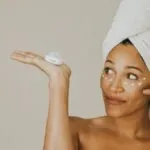 Woman holding a jar of rich face cream with dots of cream on her cheeks