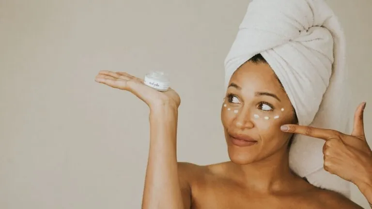 Woman holding a jar of rich face cream with dots of cream on her cheeks